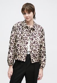 Bēšas krāsas apgriezta jaka ar leoparda rakstu un violets akcentiem, ar apkakli un pogu aizdari, kombinēta ar melniem biksēm.