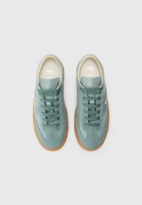 Light blue sneakers made of suede and smooth leather, featuring a textured surface, round laces, and a tan rubber sole. Gold branding detail.