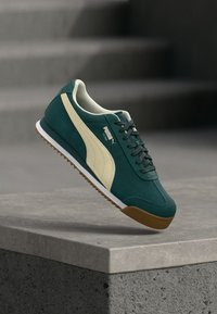 Sneakers med en mörkgrön mockaöverdel, krämfärgad sidremsa och bruna gummisulor. Har snörningsdesign och vadderad krage för komfort.