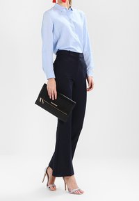 Camicia azzurra chiara con bottoni, pantaloni sartoriali blu navy, pochette nera con zip dorata e tacchi alti azzurri chiari con cinturini.