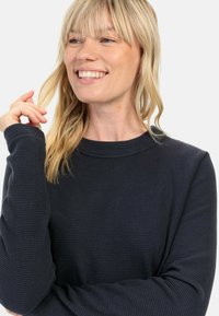 Marineblå waffle-strikket langærmet top med rund halsudskæring og afslappet pasform. Har ribbede manchetter og en struktureret overflade. Ingen synlige logoer.