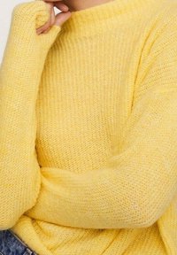 Gelbes Strickpullover mit hohem Kragen und langen Ärmeln. Der Stoff wirkt weich und strukturiert und hat eine lässige Passform.