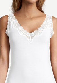 White tank top featuring a deep V-neckline with delicate lace trim along the edges and wide lace straps. Soft, smooth fabric texture.