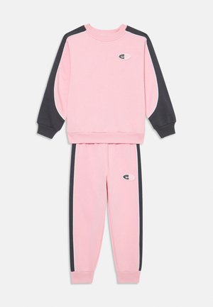 Rozā sporta krekls un bikses ar tumši pelēkiem akcentiem, ribotām attiecēm un izšūtu logo uz krūškurvja un augšstilba. Gluda tekstūra.