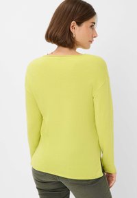 Langärmliger, leuchtend limegrüner Pullover mit weicher Textur, Rundhalsausschnitt und seitlichen Schlitzen für optimale Bewegungsfreiheit.