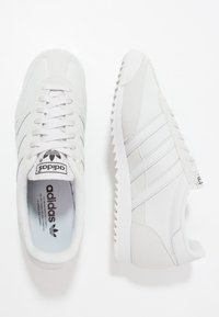 Weiße Leinenschuhe mit runden Zehen, strukturiertem Nähen, drei seitlichen Streifen und einem Zickzack-Sohlenmuster. Adidas-Logo auf der Zunge.