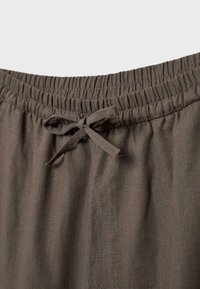 Pantalon en tissu marron avec taille élastique et cordon noué à l'avant, montré en gros plan.