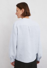 Jasnoniebieska lniana koszula z długim rękawem i luźnym krojem. Posiada plecy z zakładką oraz mankiety zapinane na guziki. Gładka tekstura, minimalistyczny design.