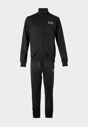Μαύρο φόρμα από λείο, ελαφρύ ύφασμα. Ζακέτα με φερμουάρ και ριμπ μανσέτες, συνδυασμένη με στενά παντελόνια που έχουν λογότυπο.