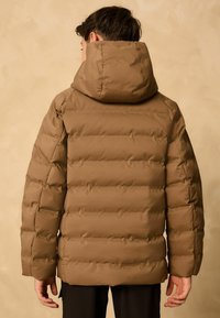Doudoune marron avec capuche, présentant des sections matelassées et des poignets élastiques. Fini lisse et mat avec une coupe légèrement ample.