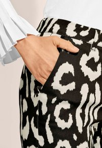 Schwarz-weiße Leopardenmuster-Hosen mit glatter Textur, ausgestattet mit einer Seitentasche und einem körperbetonten Bund. Ein weißer Rüschensleeve ist sichtbar.