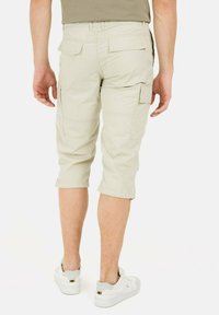 Beige cargo shorts med en afslappet pasform, der har sidelommer og baglommer, opfoldede kanter og et let, tekstureret stof. Bæres med hvide sko.