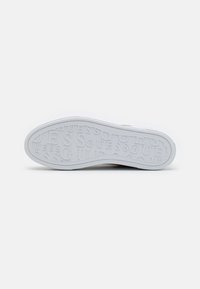 Witte sneakerzool met verhoogd "GUESS" merkpatroon, gladde textuur en een licht gebogen rand voor verbeterde grip en duurzaamheid.