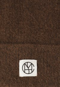 Tissu en laine marron avec une surface texturée, présentant une étiquette blanche avec un logo circulaire et une inscription noire.