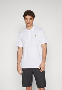 White polo shirt with a collar, short sleeves, and a yellow butterfly logo on the left chest. Paired with dark shorts.