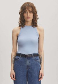 Hellblaues geripptes Tanktop mit hohem Kragen, kombiniert mit hochgeschnittenen blauen Jeans und einem schwarzen Gürtel mit einer silbernen Schnalle.