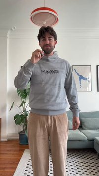 Gray hooded sweatshirt with a textured design and black printed logo. Paired with light beige corduroy pants. Indoor setting with plants.