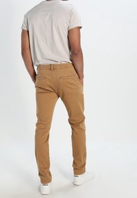 Světle šedé tričko spárované s khaki chinos kalhotami, které mají slim fit a zadní kapsy. Model nosí bílé tenisky s černými akcenty.