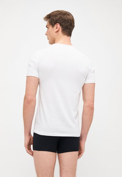 White short-sleeve T-shirt with a crew neck, smooth cotton texture, fitted design, worn with black boxer shorts. Back view, plain without graphics.