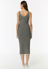 Schwarz-weiß gestreiftes Midi-Kleid mit V-Ausschnitt, taillierter Silhouette und ärmellosem Design. Kombiniert mit weißen Schuhen mit metallischen Akzenten.