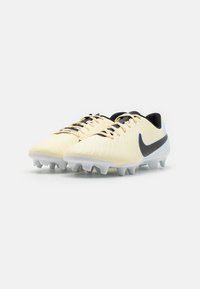 Yellow synthetic soccer cleats with textured surface, black laces, and a black swoosh logo. Outsole features white studs for traction.