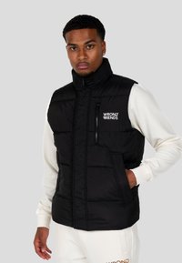 Gilet in nylon nera con collo alto, tasca sul petto con zip e tasche frontali. Presenta il logo sul lato sinistro. Leggero, con texture trapuntata.