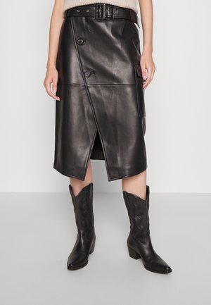 Zwarte leren midi-rok met een overslagontwerp, knoopdetails en een zijzak. Gecombineerd met zwarte cowboylaarzen met decoratieve stiksels.