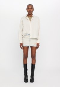 Cămașă lungă bej deschis, băgată într-o fustă mini din denim deschis. Botine negre până la genunchi completează look-ul. Design simplu și curat.