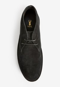 Black suede shoe with a smooth texture, featuring a round toe, stitched accents, and laces. Logo visible inside the shoe.