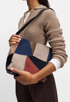Suedes handbag med geometriskt lapptäcke i nyanser av blått, beige och rött. Inkluderar ett svart handtag och gulddetaljer.