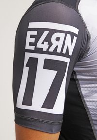 Krátký rukáv sportovní tričko v černé a šedé barvě. Obsahuje bíle potištěný text "E4RN" a "17" na levém rukávu. Hladký, elastický materiál.