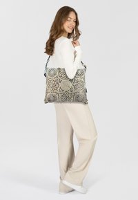 Gran bolsa tote que presenta un patrón geométrico en beige y negro, con acentos texturizados y una resistente correa para el hombro.