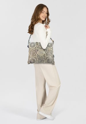 Grand tote bag avec un motif géométrique beige et noir, des accents texturés et une bandoulière robuste.