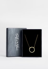 Collana d'oro con un pendente circolare decorato con piccole gemme, esposta in una elegante scatola di gioielli foderata in velluto scuro con un esterno argentato.