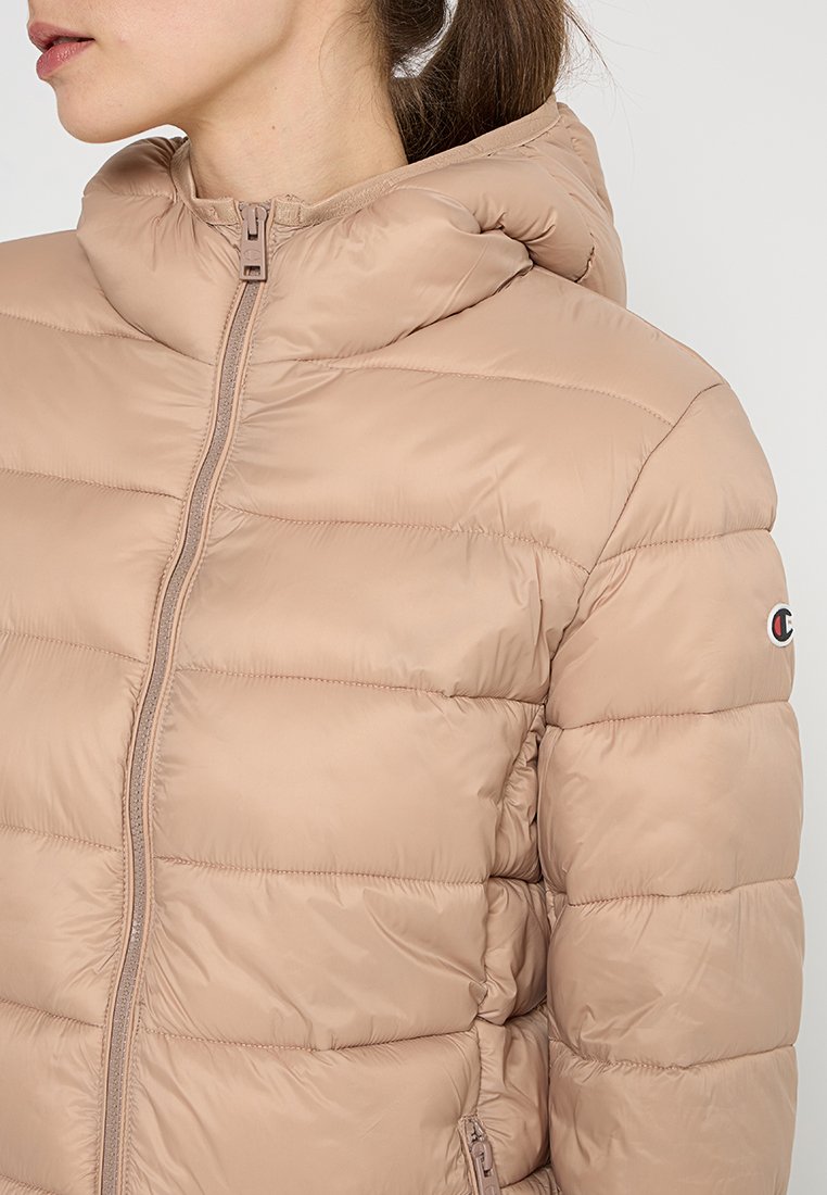 Giacca a vento beige con cappuccio, con texture trapuntata, chiusura frontale con zip e un piccolo logo sulla manica sinistra.