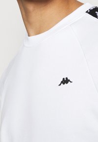 Witte sweatshirt met ronde hals, van katoen, met een zwart geborduurd logo op de linkerborst en patronen op de schouder.