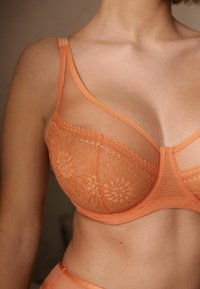 Pomarańczowa bielizna z prześwitującą siateczką i kwiecistymi koronkami. Posiada regulowane ramiączka oraz gładki pas. Delikatne rzemiosło widoczne w detalu.