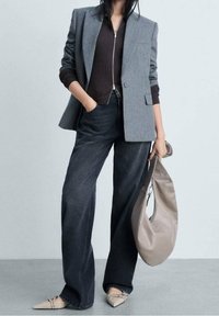 Blazer gris, pull côtelé marron foncé, jean taille haute foncé, sac à main beige clair et ballerines pointues à motif. Look globalement moderne.