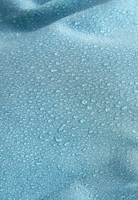 Helles blaues Gewebe mit einer weichen Textur, das zahlreiche kleine Wassertropfen auf der Oberfläche zeigt und damit seine wasserabweisenden Eigenschaften unterstreicht.