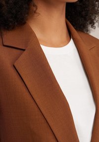 Brown tailored blazer with a textured finish, featuring notched lapels and paired with a plain white T-shirt underneath.