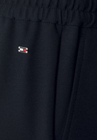 Czarne sportowe spodnie wykonane z miękkiej tkaniny z elastycznym paskiem w talii. Posiadają małą naszywkę z logo w czerwono, białym i niebieskim kolorze.