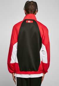 Piros és fekete dzseki fehér díszítéssel, magas gallérral, bordás aljjal és logós matricával a hátsó részen. Sleek, texturált anyag.
