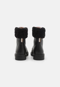 Stivali neri in pelle fino alla caviglia con finitura testurizzata, un morbido risvolto nero e un sottile dettaglio beige sul retro. Design minimalista con una suola robusta.
