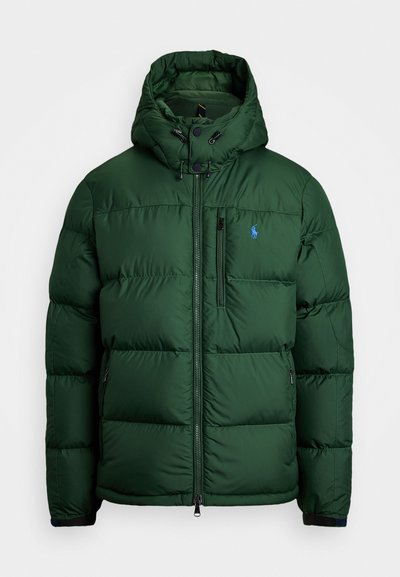 Ciemnozielona kurtka puchowa z wysokim kołnierzem i odpinanym kapturem. Posiada czarne kieszenie zapinane na zamek i małe niebieskie logo na klatce piersiowej.