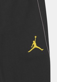 Černé tepláky s vyšitým žlutým logem Jumpman, s šedými švy a měkkou, hladkou texturou látky.