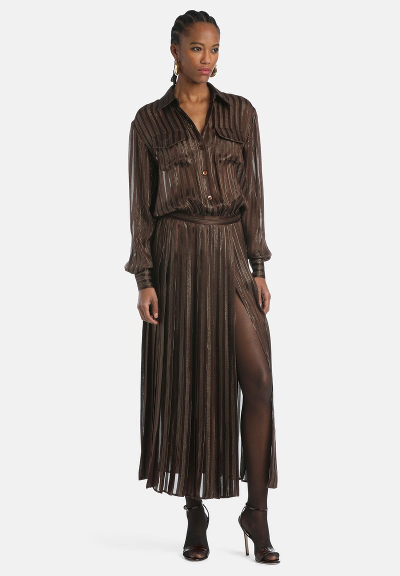 Vestido marrón con plisados, escote de camisa abotonada, mangas largas y una abertura alta en el muslo. Presenta tiras metálicas y un cinturón a juego.