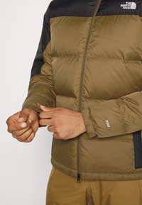 Padded jacka i olivgrön med svarta axlar, med en framsidans dragkedja, elastiska muddarna och "700" tryckt på ärmen. Maskintvättbart tyg.