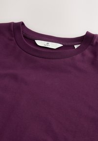 Tamnoljubičasta majica od pamuka s okruglim izrezom i bijelom NEXT etiketom ušivenom iznutra na ovratniku.