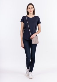 Marineblaues T-Shirt, kurze Ärmel; dunkle Jeans; hellgraue Umhängetasche; weiße Sneakers. Schlichtes Design mit lässigem Schnitt und glatter Textur.