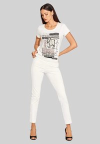 Witte T-shirt met grafische prints in zwart en taupe. Gecombineerd met witte slim-fit broek en zwarte openteenhakken.